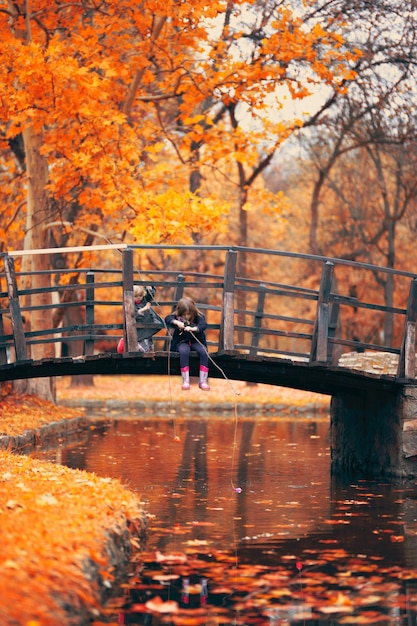 Zdjęcie siostry łowią ryby w rzece, siedząc na moście dla pieszych przeciwko drzewom jesieni w parku