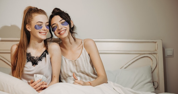 Siostry Rasy Białej Siedzą W łóżku I Noszą Maski Przeciwzmarszczkowe Pod Oczami Podczas Picia Herbaty