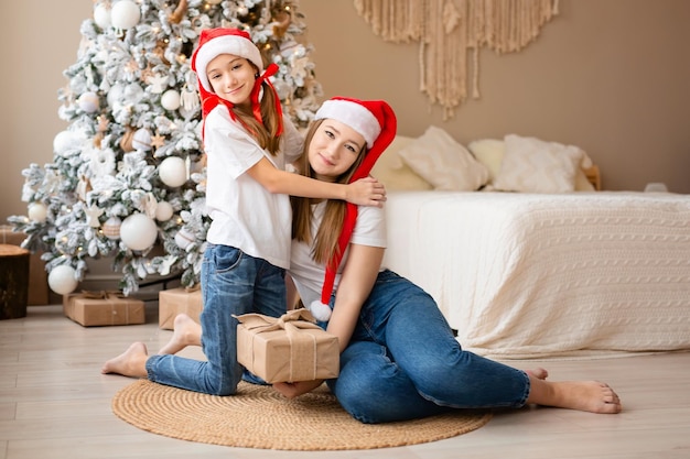 Siostry świętują wakacje zimowe dziewczęta wymieniają prezenty świąteczne w pobliżu choinki szczęśliwe wśród nowych