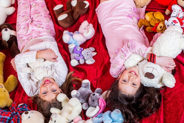 Zdjęcie siostry w piżamach leżą w łóżku, dzieci w miękkich, ciepłych piżamach bawią się w domu.