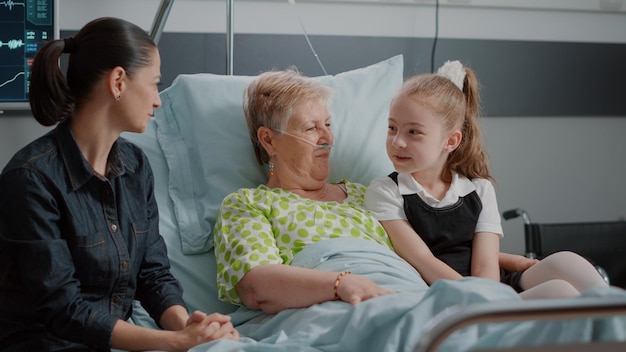 Siostrzenica i chora babcia przytulają się podczas wizyty rodziny na oddziale szpitalnym. Mała dziewczynka rozmawia i przytula się ze starszym chorym pacjentem, odwiedzając matkę. Odwiedzający na sali intensywnej terapii