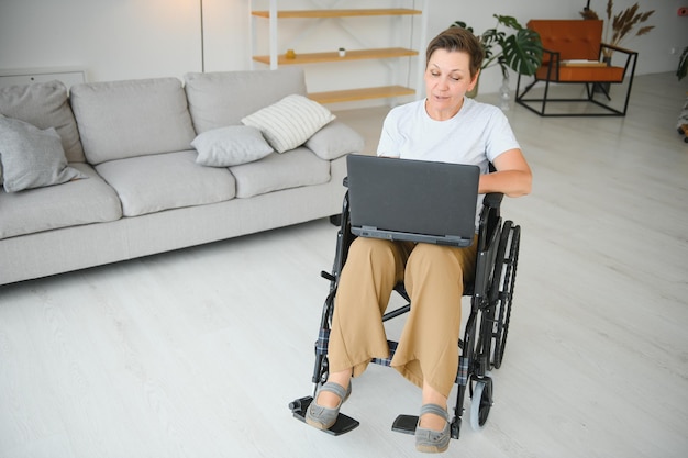 Siwowłosa niepełnosprawna kobieta w średnim wieku prowadzi wideorozmowę siedzącą na wózku inwalidzkim w domu