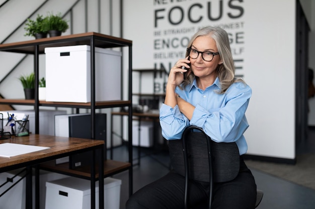 Siwowłosa starsza kobieta biznesu w średnim wieku rozmawia przez telefon w biurze pracuje z zastrzeżeniami