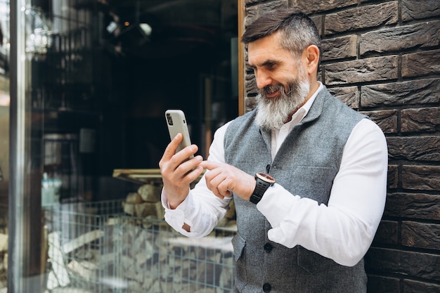 Siwowłosy brodaty starszy mężczyzna używa i rozmawia przez smartfon