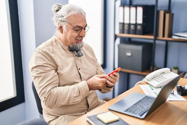 Siwowłosy mężczyzna w średnim wieku, pracownik biznesowy korzystający z laptopa i smartfona w biurze