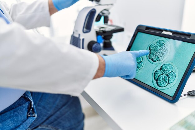 Zdjęcie siwowłosy mężczyzna w średnim wieku, ubrany w mundur naukowca, wyglądający na touchpad obrazu embriologicznego w laboratorium