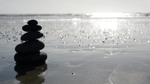 Zdjęcie skała równoważąca oceaniczną plażę, kamienie układające się przez fale wody morskiej. piramida kamyków na piaszczystym brzegu