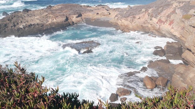 Skalista, skalista plaża oceaniczna. Wielkie fale rozbijające się o nagi klif, niebieska woda pluska, morska piana. Siła natury w pobliżu Big Sur, 17 mil jazdy. Dramatyczny pejzaż morski. Point Lobos, Monterey, wybrzeże Kalifornii, USA