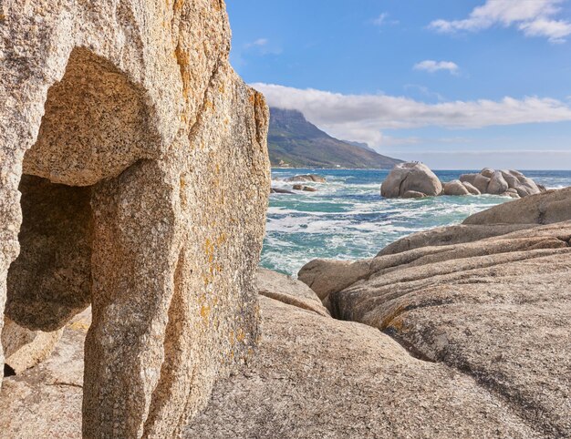 Skalisty brzeg i morski widok na ocean z błękitnym niebem i górą w tle w Camps Bay Cape Town RPA Spokojna, spokojna plaża i sceneria przyrody