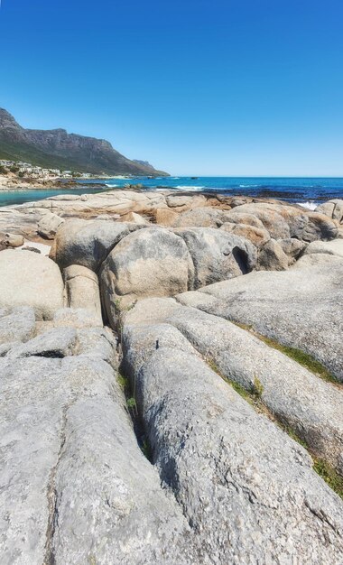 Skalisty krajobraz prowadzący do morza pod zachmurzonym błękitnym niebem kopia miejsce na plaży Camps Bay Cape Town Republika Południowej Afryki Głazy na wybrzeżu z górą Dwunastu Apostołów w tle