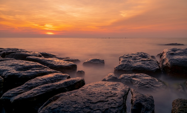 Skały na kamień plaży o zachodzie słońca. Piękne niebo zachód słońca na plaży. Zmierzch morze i niebo. Tropikalne morze o zmierzchu. Dramatyczne niebo i chmury.