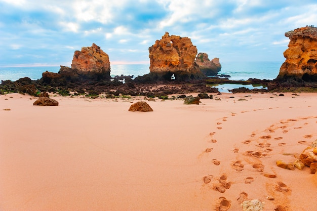 Skały na piaszczystej plaży w Algarve, Portugalia. Wybrzeże Oceanu Atlantyckiego, lato seascape. Ślady stóp na piasku