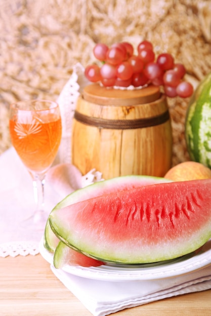 Zdjęcie skład dojrzałych owoców arbuza różowego wina w szklanej i drewnianej beczce na kolorowym drewnianym stole na tle ściany koloru