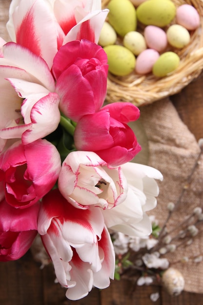 Skład z Wielkanocnymi jajkami i pięknymi tulipanami w szklanym dzbanku na drewnianym tle