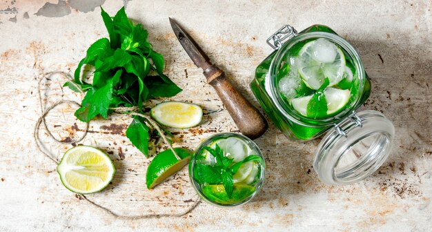 Składniki do robienia mojito - limonka, liście mięty, rum, nóż do cytrusów i stary stół.