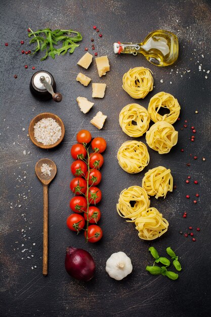 Składniki na tradycyjne włoskie danie z makaronu. Niegotowane surowe tagliatelle bolognesi, parmezan, oliwa z oliwek, czosnek, liście bazylii, papryka, pomidorki koktajlowe. Widok z góry