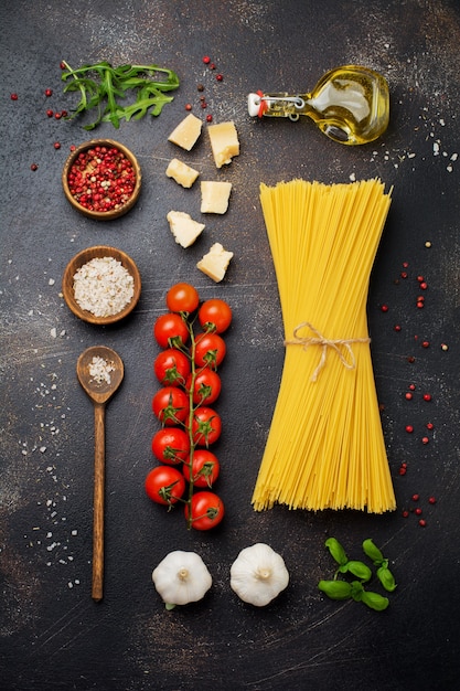 Składniki na tradycyjne włoskie danie z makaronu. Surowe spaghetti niegotowane, parmezan, oliwa z oliwek, czosnek, liście bazylii, papryka, pomidorki koktajlowe. Top