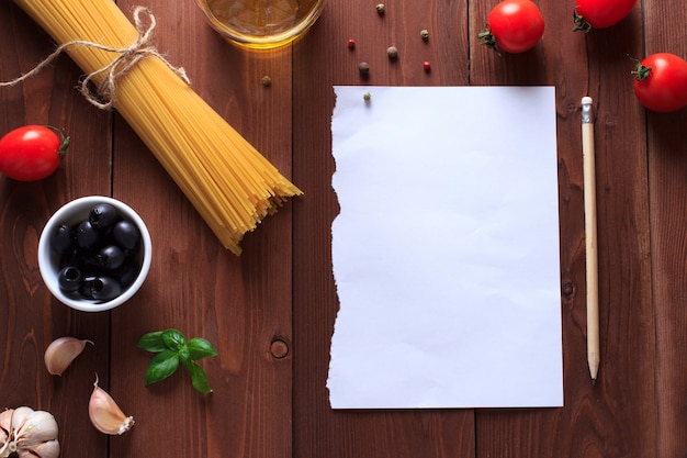 Składniki na włoski makaron na drewnianym stole z papieru do pisania receptur.