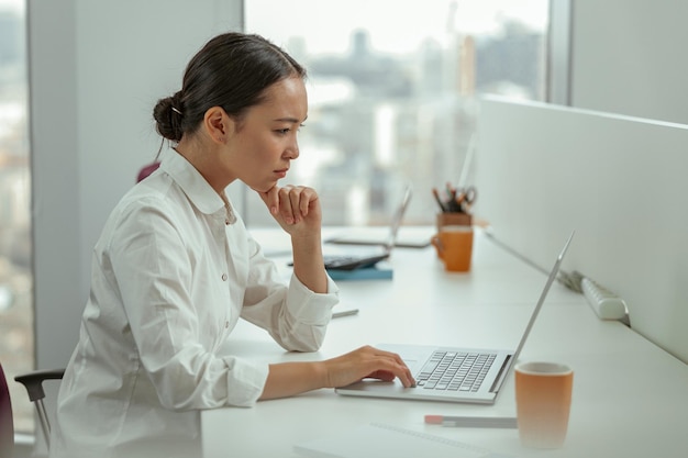 Zdjęcie skoncentrowana azjatycka biznesowa kobieta pracująca na laptopie siedząca w nowoczesnym biurze