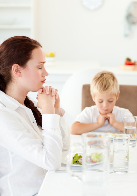 skoncentrowana matka i syn modlący się podczas lunchu