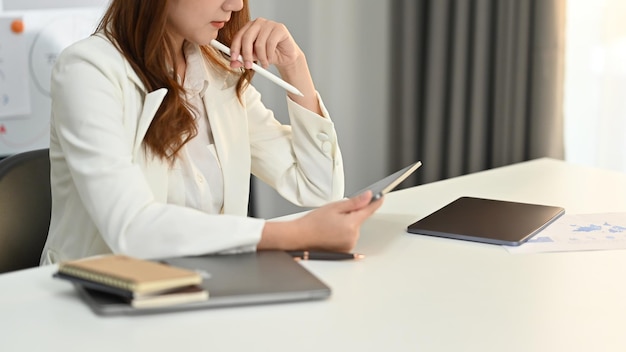 Skoncentrowana Milennila CEO firmy w eleganckim garniturze za pomocą tabletu cyfrowego w swoim miejscu pracy