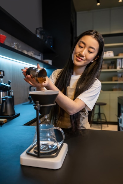 Zdjęcie skoncentrowana młoda barista dodawa kawy do lejek do kawiarni z filtrem