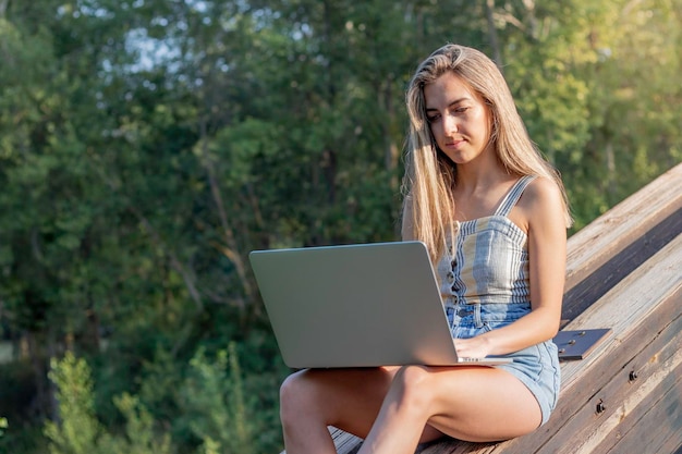 Skoncentrowana młoda kobieta pracująca online jako grafik na swoim laptopie w otoczeniu przyrody i przestrzeni kopiowania