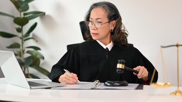 Skoncentrowana starsza prawniczka w szlafrokowym mundurze siedząca przed laptopem, zapewniająca konsultacje prawne i porady prawne online