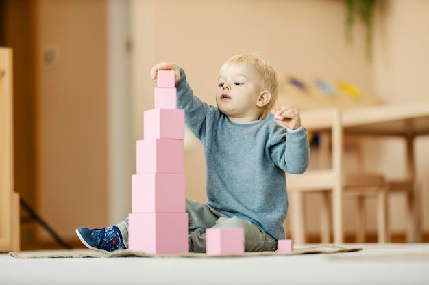 Zdjęcie skoncentrowane dziecko kładzie klocki i buduje wieżę w przedszkolu montessori