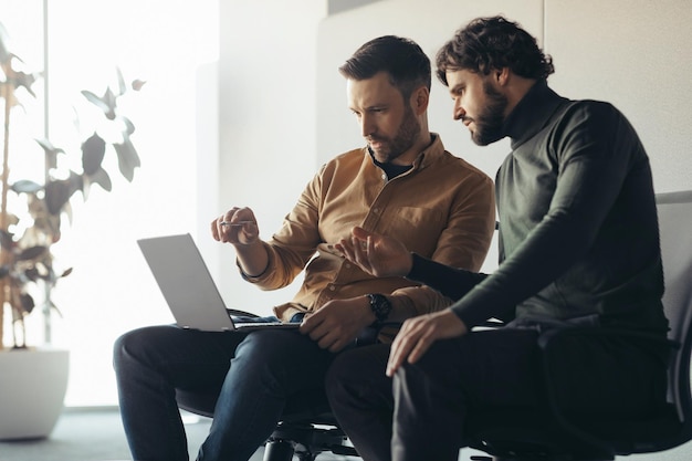 Zdjęcie skoncentrowani pracownicy firmy patrzący na ekran laptopa, pracujący wspólnie nad projektem biznesowym w nowoczesnym stylu