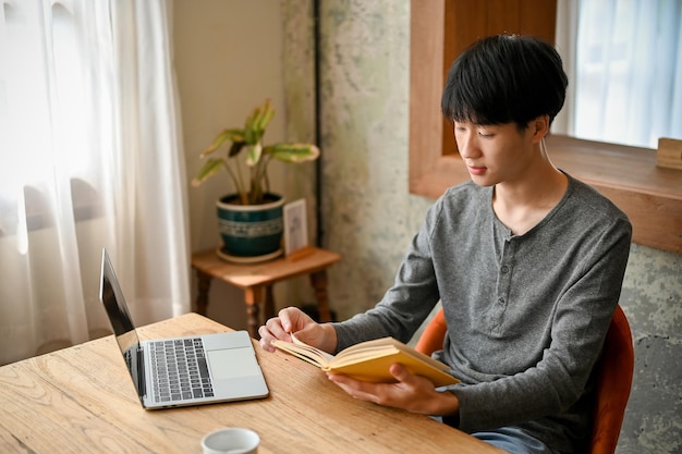 Skoncentrowany azjatycki student college'u czyta książkę lub podręcznik zdalnie pracujący w kawiarni