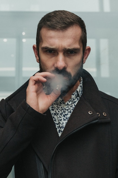 Zdjęcie skoncentrowany brodaty biznesmen pali papierosa i poważnie