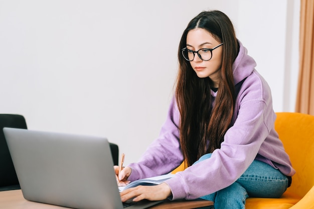 Skoncentrowany Kaukaski Młoda Studentka College'u Kobieta W Okularach Studiuje Z Laptopem, Odlegle Przygotowuje Się Do Egzaminu Testowego, Pisze Esej, Odrabianie Lekcji W Domu, Odległa Koncepcja Edukacji.