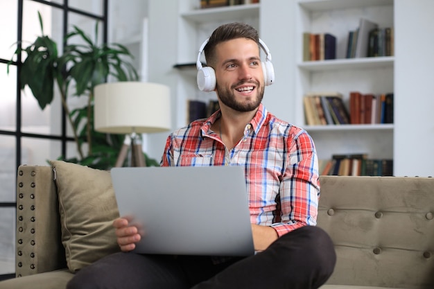 Skoncentrowany młody biznesmen freelancer siedzący na kanapie z laptopem, pracujący zdalnie online w domu.