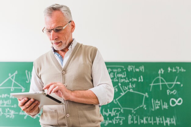 Zdjęcie skoncentrowany nauczyciel matematyki w wieku obliczania na tablecie