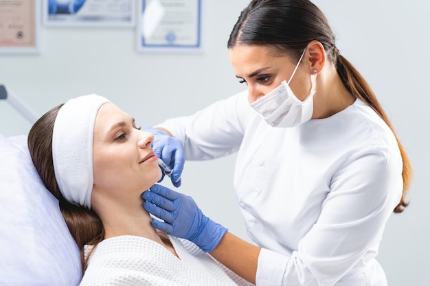 Skoncentrowany profesjonalny dermatolog kaukaski w masce na twarz zmniejszający fałdy nosowo-wargowe u pacjentki