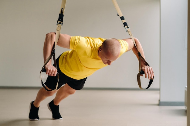 Skoncentrowany sportowiec wykonujący ćwiczenia na funkcjonalnych pętlach na siłowni.