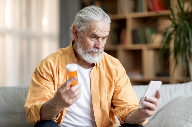 Skoncentrowany starszy mężczyzna trzymający lekarstwo i smartfon