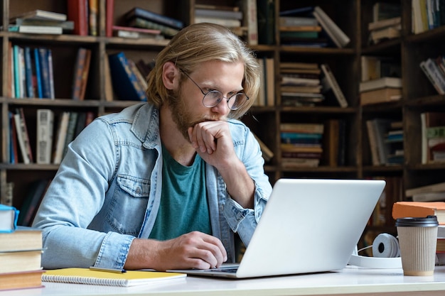 Skoncentrowany student studiuje online na komputerze, patrząc na ekran w bibliotece