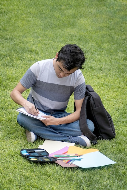 Skoncentrowany uczeń siedzący na trawie i piszący w notatniku