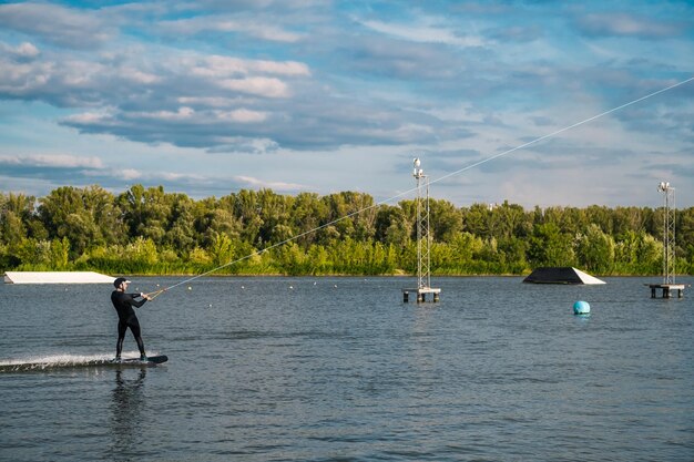 Skoncentrowany wysportowany mężczyzna jeżdżący na wakeboardzie, ciągniętym na kablu po spokojnej rzece