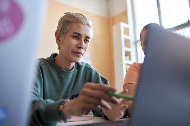 Skoncentruj się na młodym azjatyckim studencie prezentującym koledze z klasy nowy projekt lub oprogramowanie, wskazując na ekran laptopa