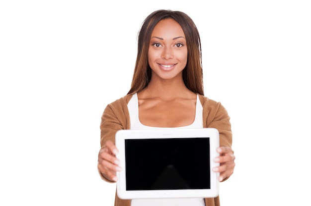 Skopiuj Miejsce Na Jej Tablecie. Piękna Młoda Afrykańska Kobieta Pokazuje Ci Swój Cyfrowy Tablet I Uśmiecha Się Stojąc Na Białym Tle