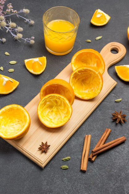 Skórka pomarańczowa na desce do krojenia. Laski cynamonu i szklankę soku pomarańczowego na stole. Czarne tło. Widok z góry