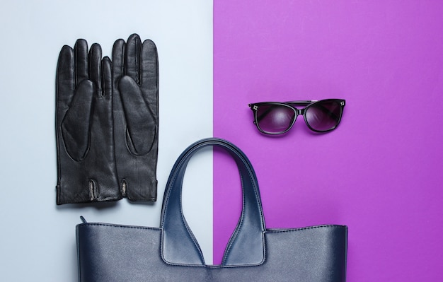 Skórzana torba, okulary przeciwsłoneczne, rękawiczki na szaro-fioletowym stole. Widok z góry