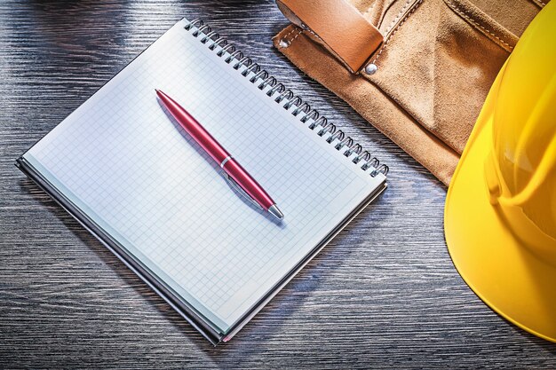 Skórzany pas budowlany kask notatnik długopis na desce.