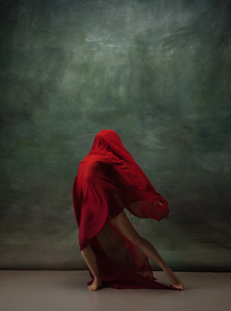 Skrzydła latające Zgrabna klasyczna baletnica tańcząca na ciemnym tle studyjnym Głęboko czerwony materiał