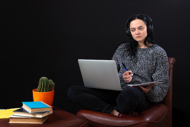 Skupiająca się młoda niezależna kobieta siedzi z laptopem i słuchawkami, pracując zdalnie online z domu