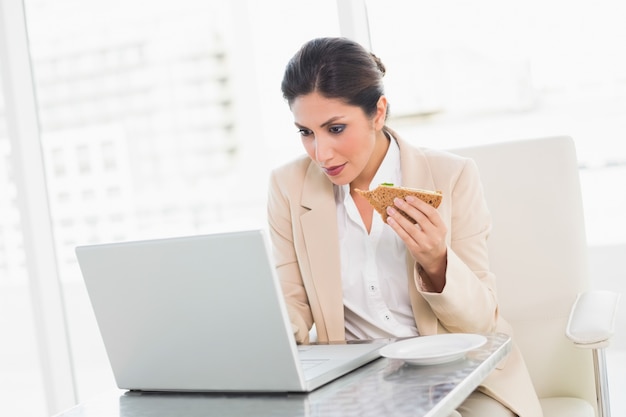 Skupiający się bizneswomanu łasowania lunch gdy pracuje