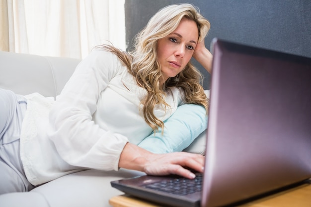 Zdjęcie skupiający się blondynki lying on the beach na leżance używać laptop